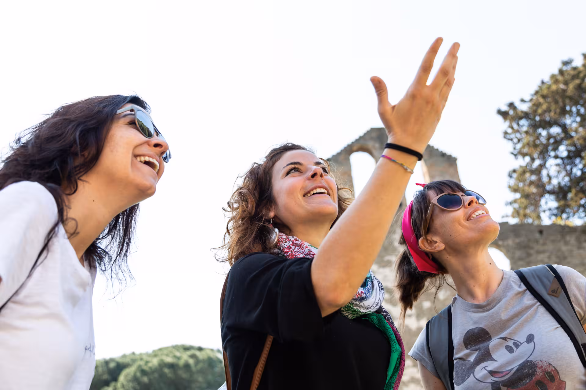 Three women enjoy a guided tour on the historic Appian Way, surrounded by ancient ruins and lush greenery.