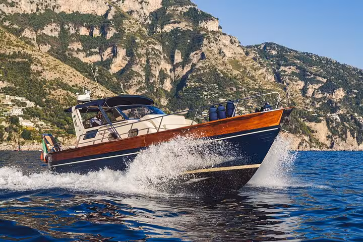Apreamare 10 boat cruising through clear blue waters near Positano with dramatic cliffs in the background.
