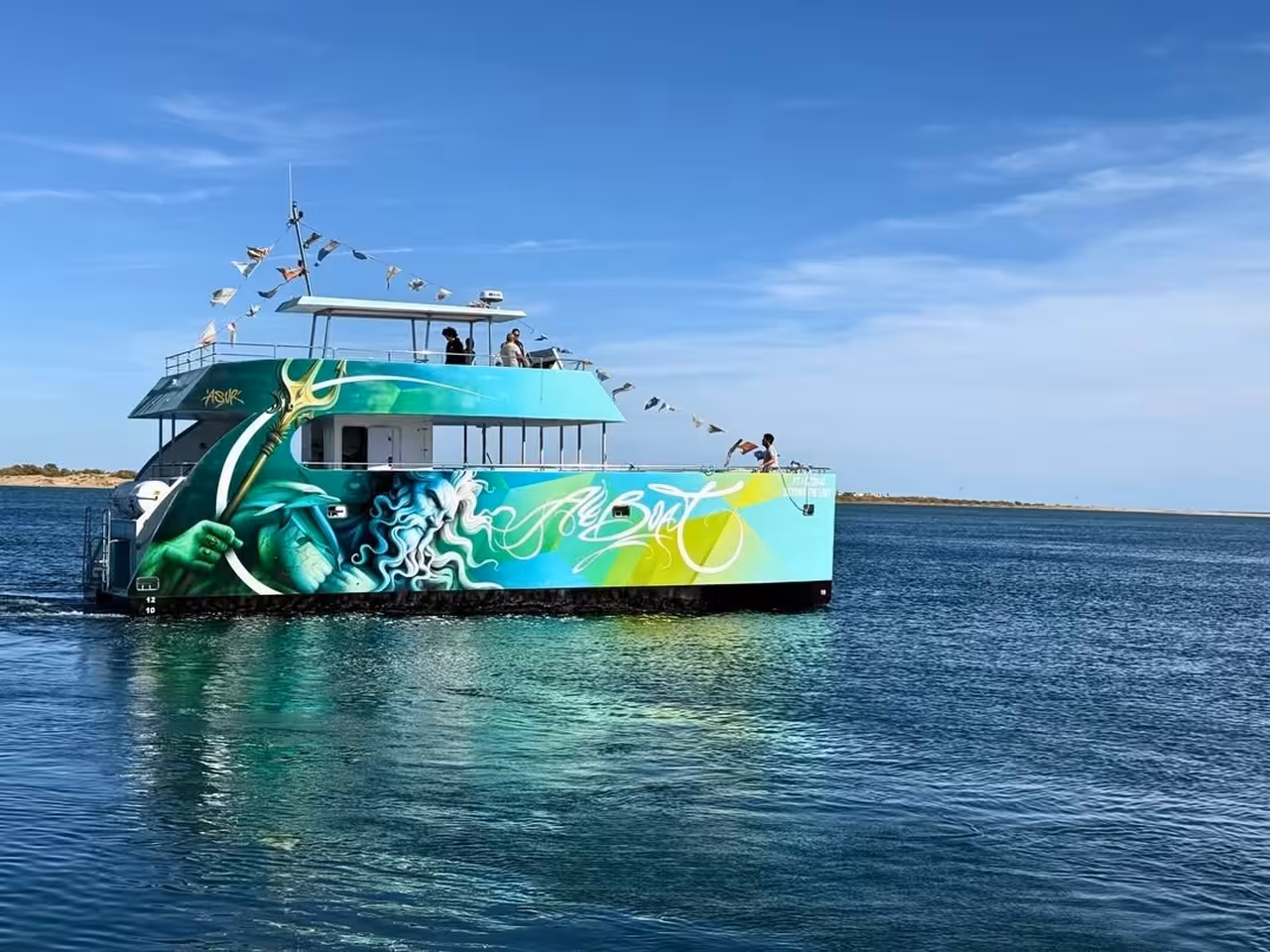 Vibrant luxury catamaran with colorful ocean-themed artwork sailing calm Algarve waters on Benagil Caves tour from Albufeira