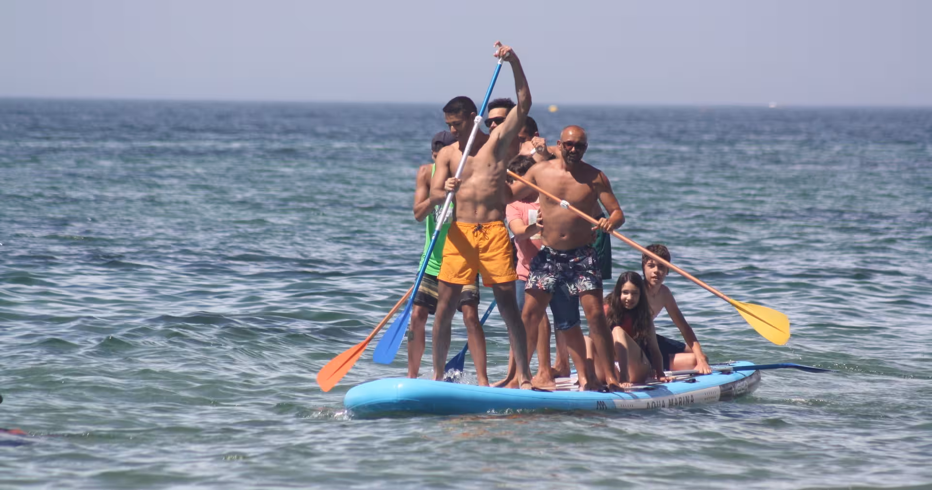 Family and friends paddling together on a giant Aqua Marina Mega SUP board during a fun group ocean adventure.