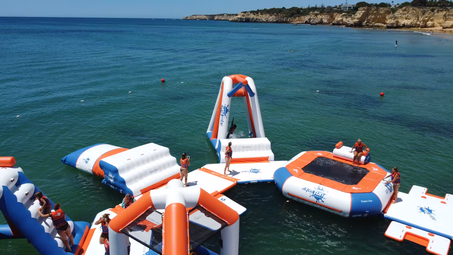 Aerial view of Aquafun inflatable waterpark with trampolines and slides floating in turquoise coastal waters