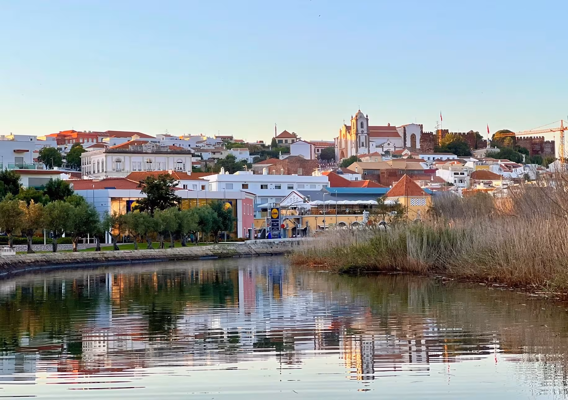 Colorful riverfront view of Silves old town and castle reflecting in the calm Arade River on a peaceful Algarve boat tour