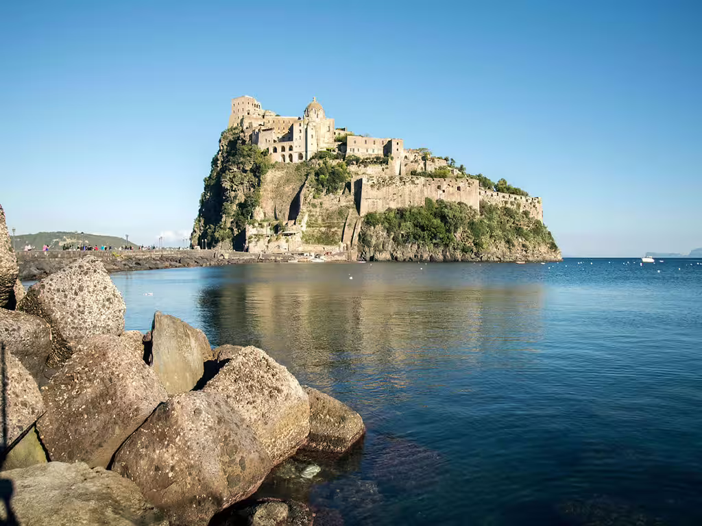 Aragonese Castle perched on a rocky islet in Ischia, Italy, viewed from the sea on a coastal boat tour
