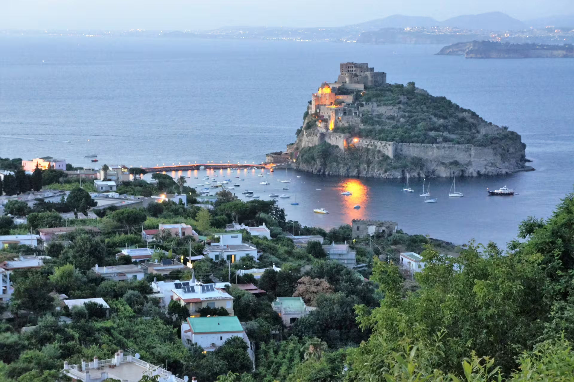 Sunset lights on Aragonese Castle in Ischia with boats in the bay, seen from a coastal cruise from Sorrento to Procida
