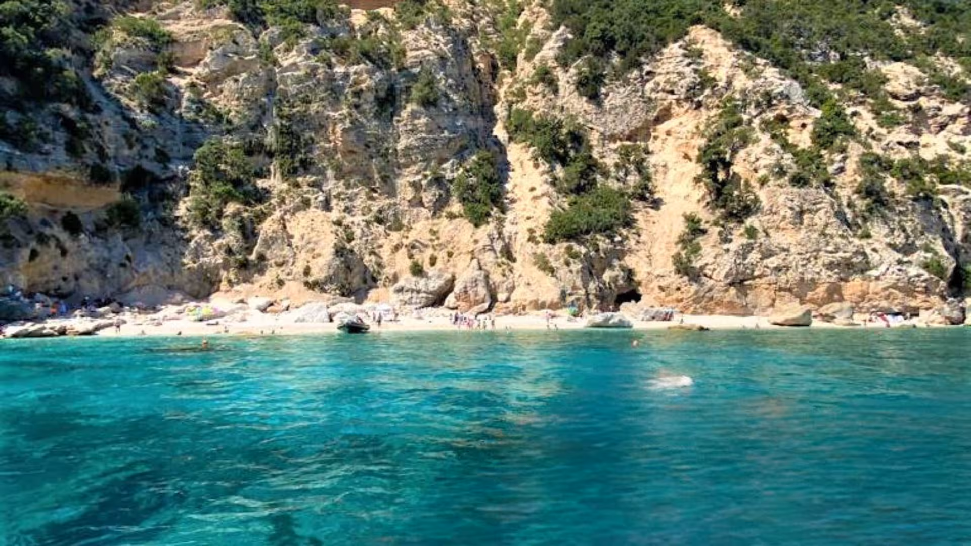 Pristine beach with clear blue waters and rocky cliffs at Cala Mariolu, perfect for a peaceful escape.