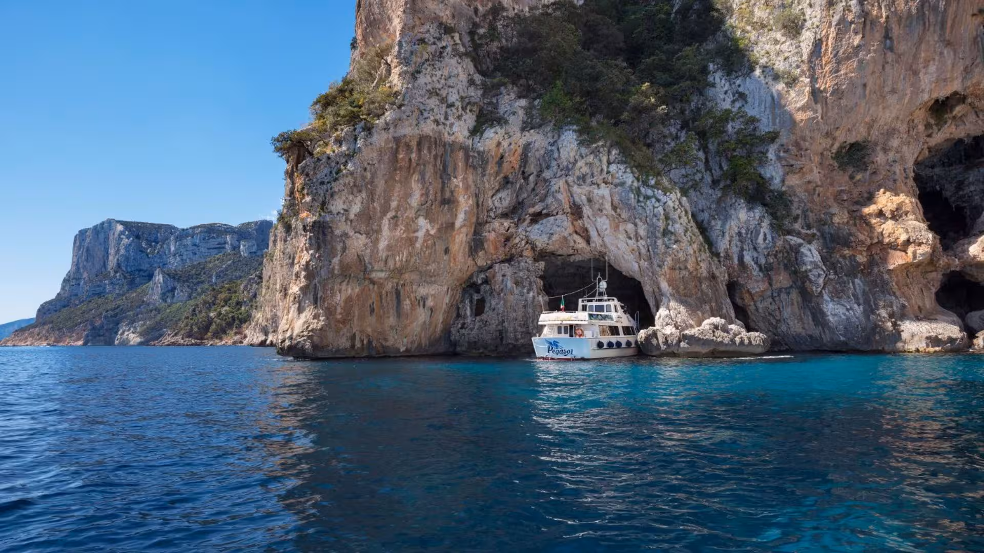 A boat navigates the scenic sea cave formations along the Gulf of Orosei's dramatic coastline, ideal for adventurous tours.