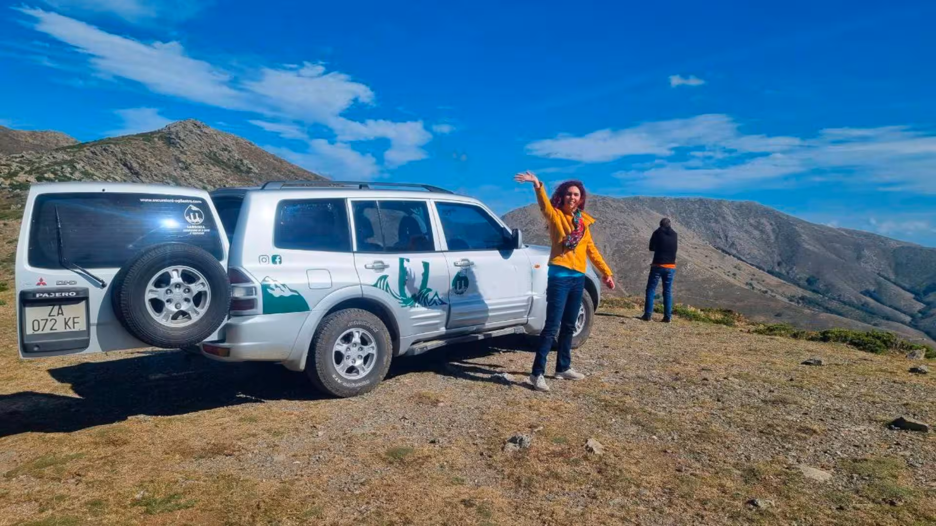 A woman waves beside a Jeep on a scenic Sardinian hilltop during a Barbagia Jeep tour.