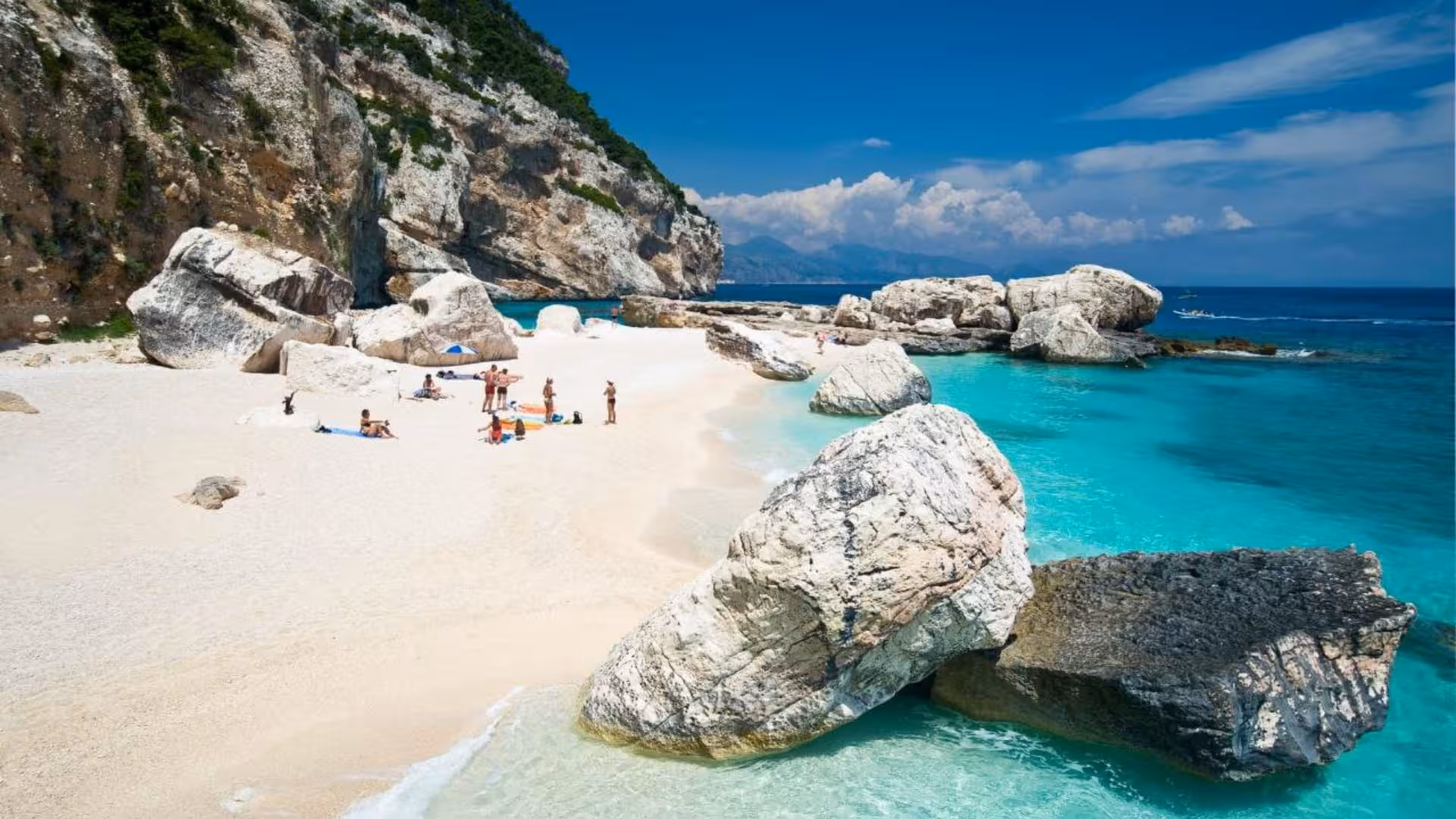 Visitors enjoying the sunny white sands and clear waters of Cala Mariolu with stunning rock formations.