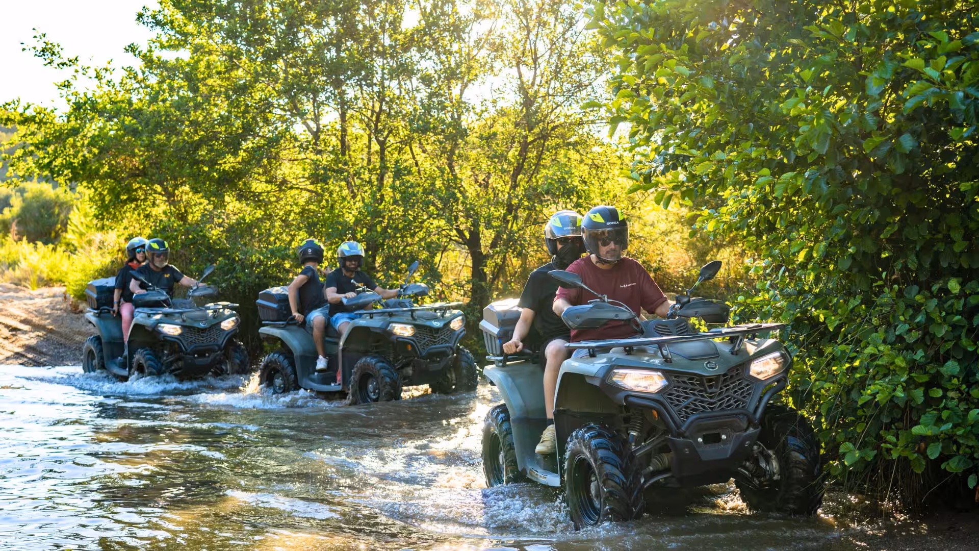 Group on ATVs crossing a shallow stream during Arbus dunes and mines excursion.