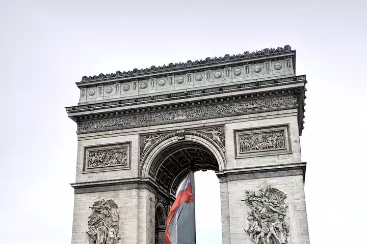 Arc de Triomphe monument with French flag and intricate stone relief sculptures in Paris