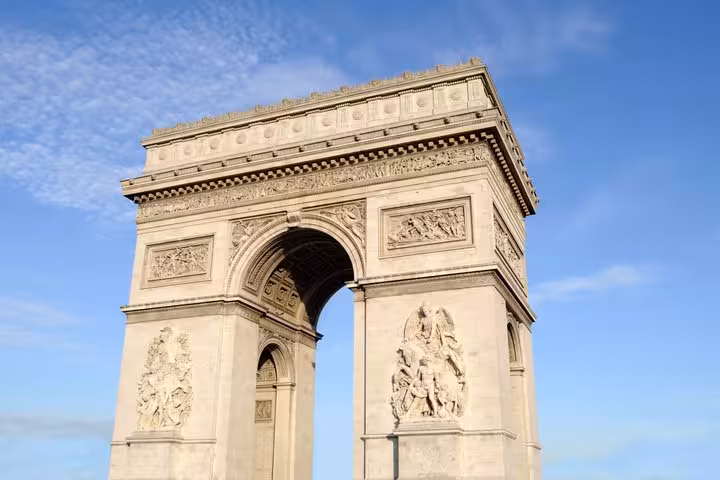 Arc de Triomphe monument with ornate stone carvings against blue sky, Paris France