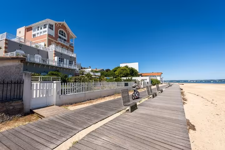 Wooden boardwalk along Arcachon beach with seafront villas and a cyclist on a sunny day