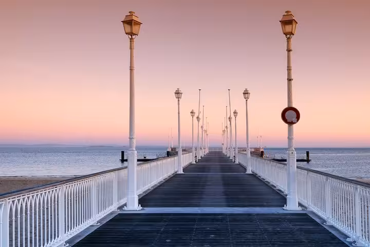 White pier with ornate lamp posts extending over calm sea at pink sunset in Arcachon, France