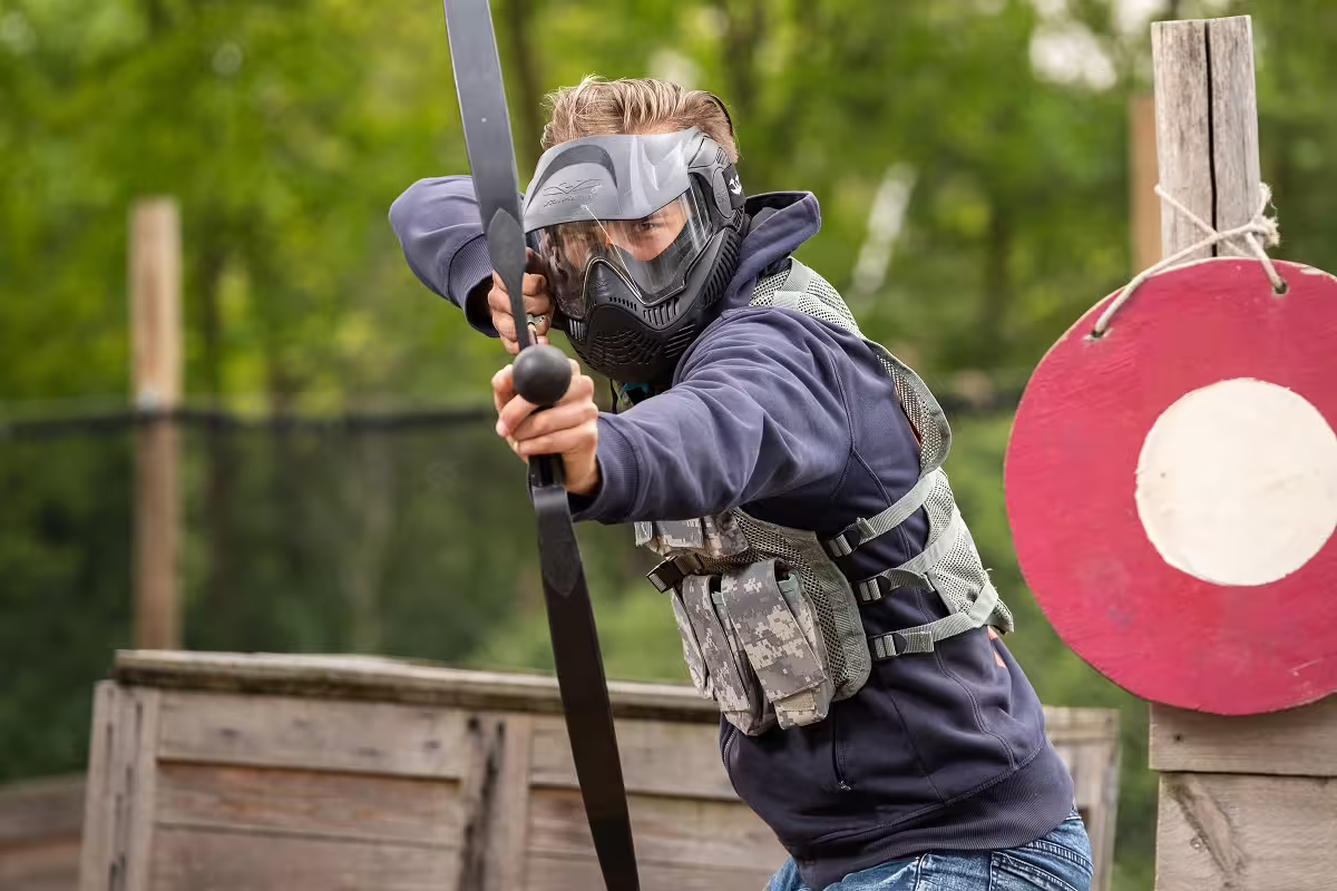 Masked player aiming bow in Archery Tag Amsterdam arena, outdoor team battle with foam arrows