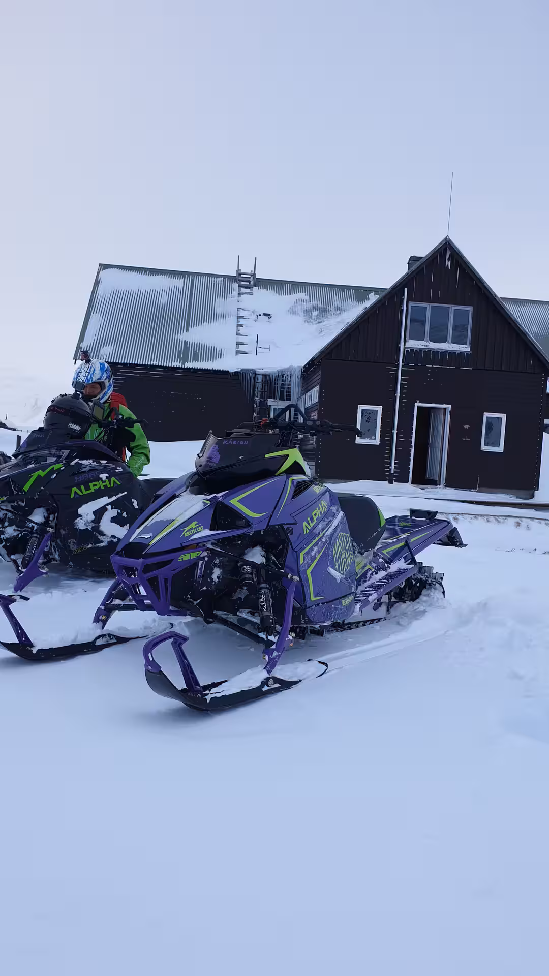 Purple Arctic Cat Alpha snowmobile parked in snow outside dark wooden mountain lodge in Landmannalaugar