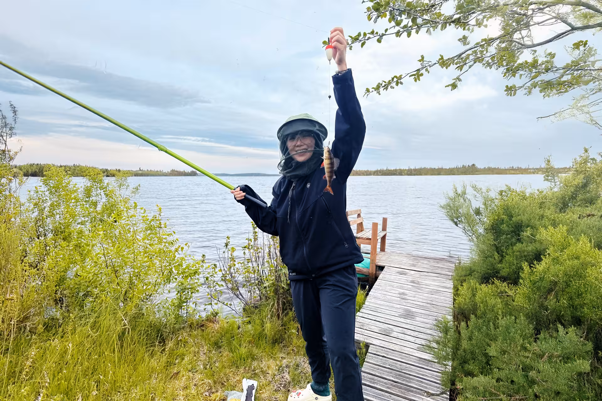 Smiling angler holding a fresh catch on a scenic lakeside dock during the Arctic Lakeside Fishing Experience in Rovaniemi.