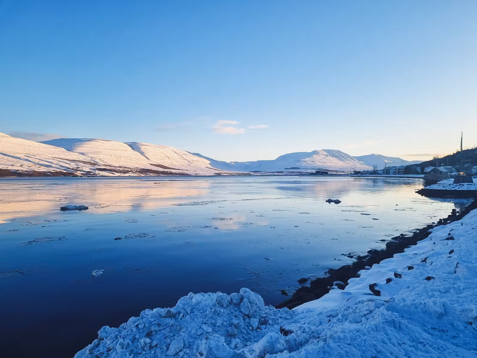 Arctic fjord with snowy mountains and icy shoreline, scenic stop on private husky and aurora borealis tour