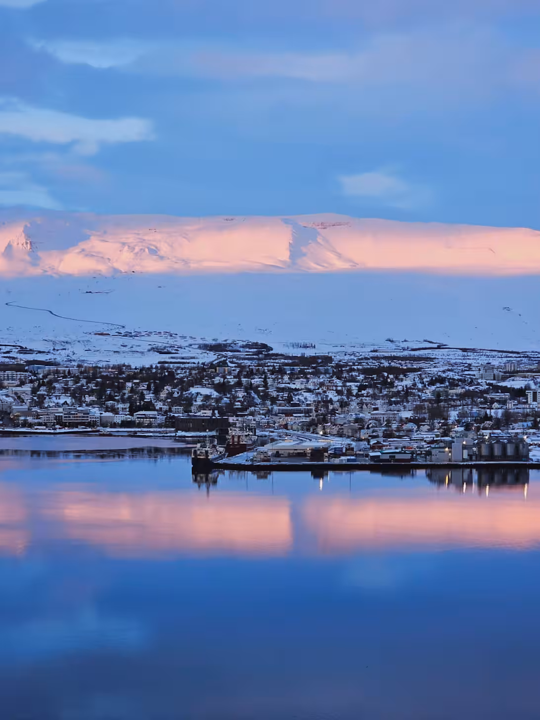 Winter coastal town and fjord at dusk with pink-lit mountains, ideal for private husky safari and aurora viewing