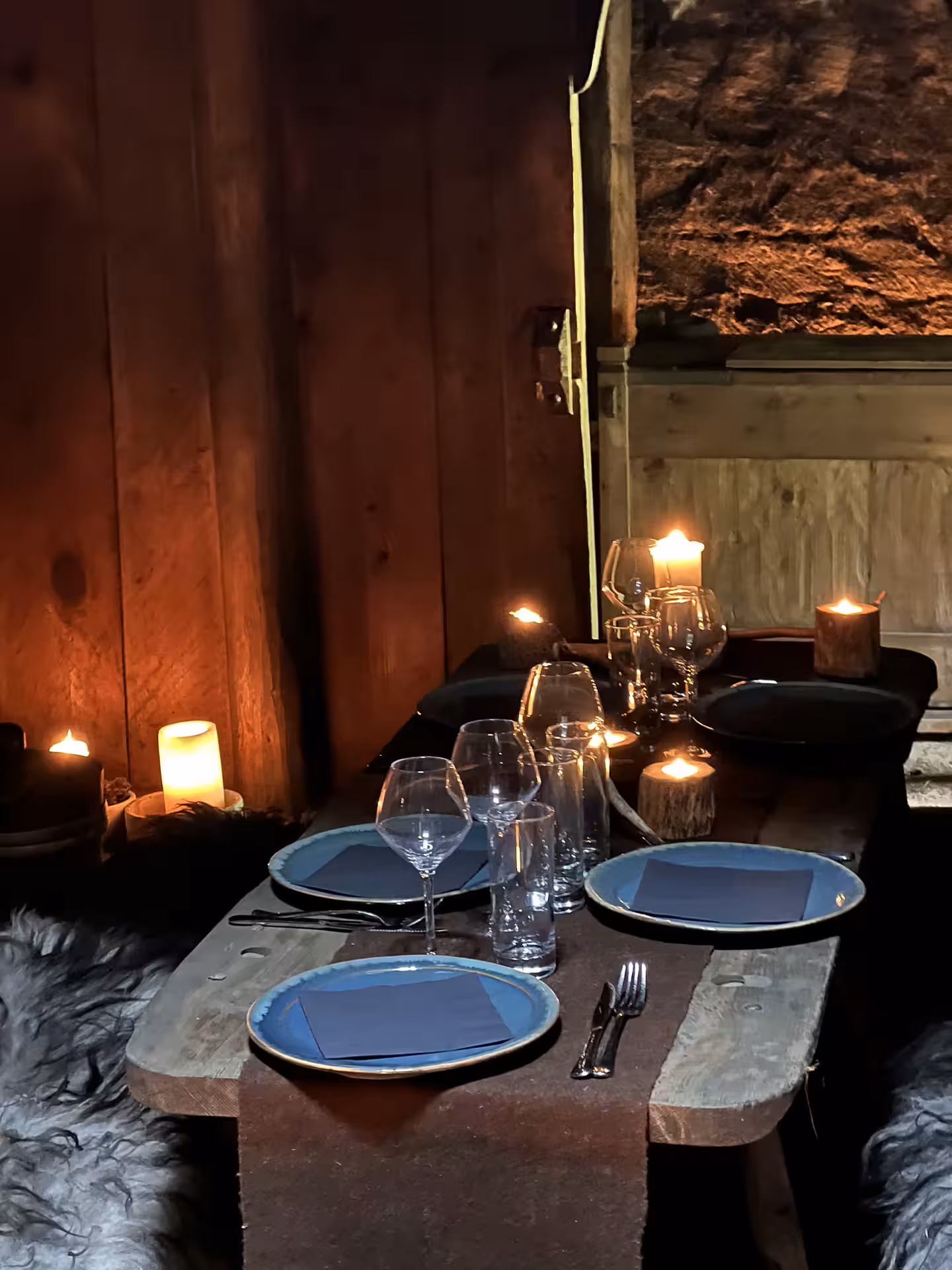 Cozy Arctic Table candlelit dinner setting with blue ceramic plates and wine glasses in a rustic wooden interior