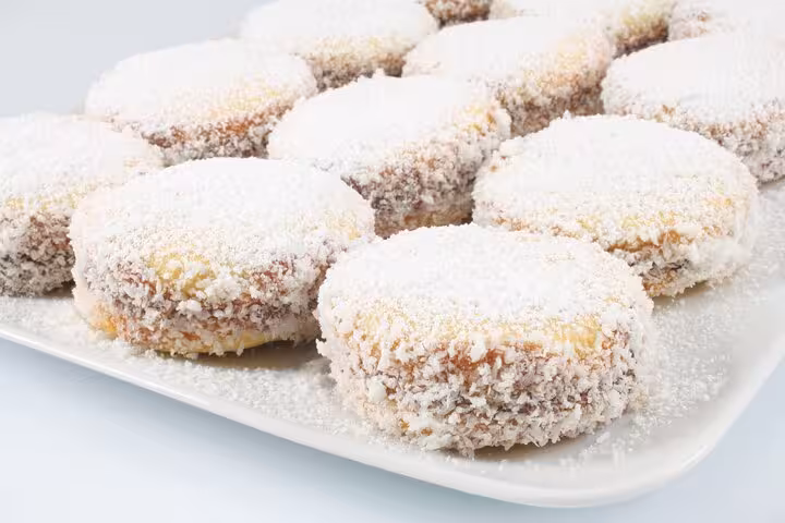 Delicious Argentinian alfajores dusted with coconut and powdered sugar, elegantly arranged on a white platter.