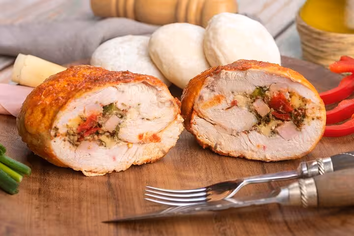 Sliced Argentinian stuffed chicken roll with herbs and peppers, surrounded by fresh ingredients on a wooden board.
