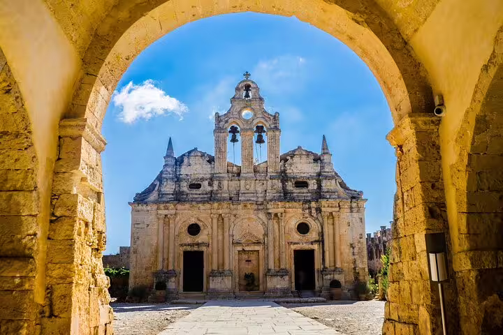 Arkadi Monastery's grand entrance framed by an ancient stone archway under a clear blue sky.