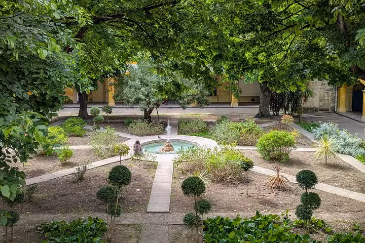 Lush garden courtyard with central fountain and trimmed shrubs in Arles, France