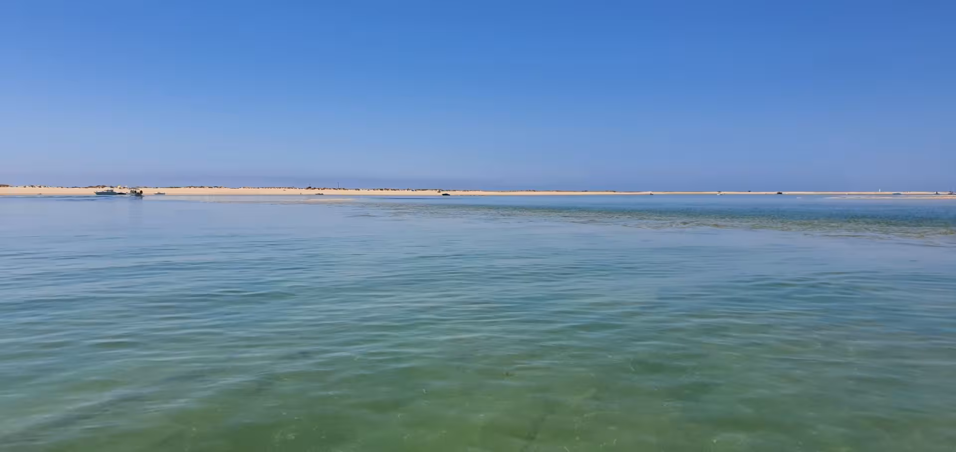 Tranquil sea view from Deserted Beach showcasing clear turquoise waters and a distant sandy coastline under a bright sky.