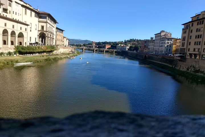 View of the Arno River in Florence with historic buildings lining both banks under a clear blue sky