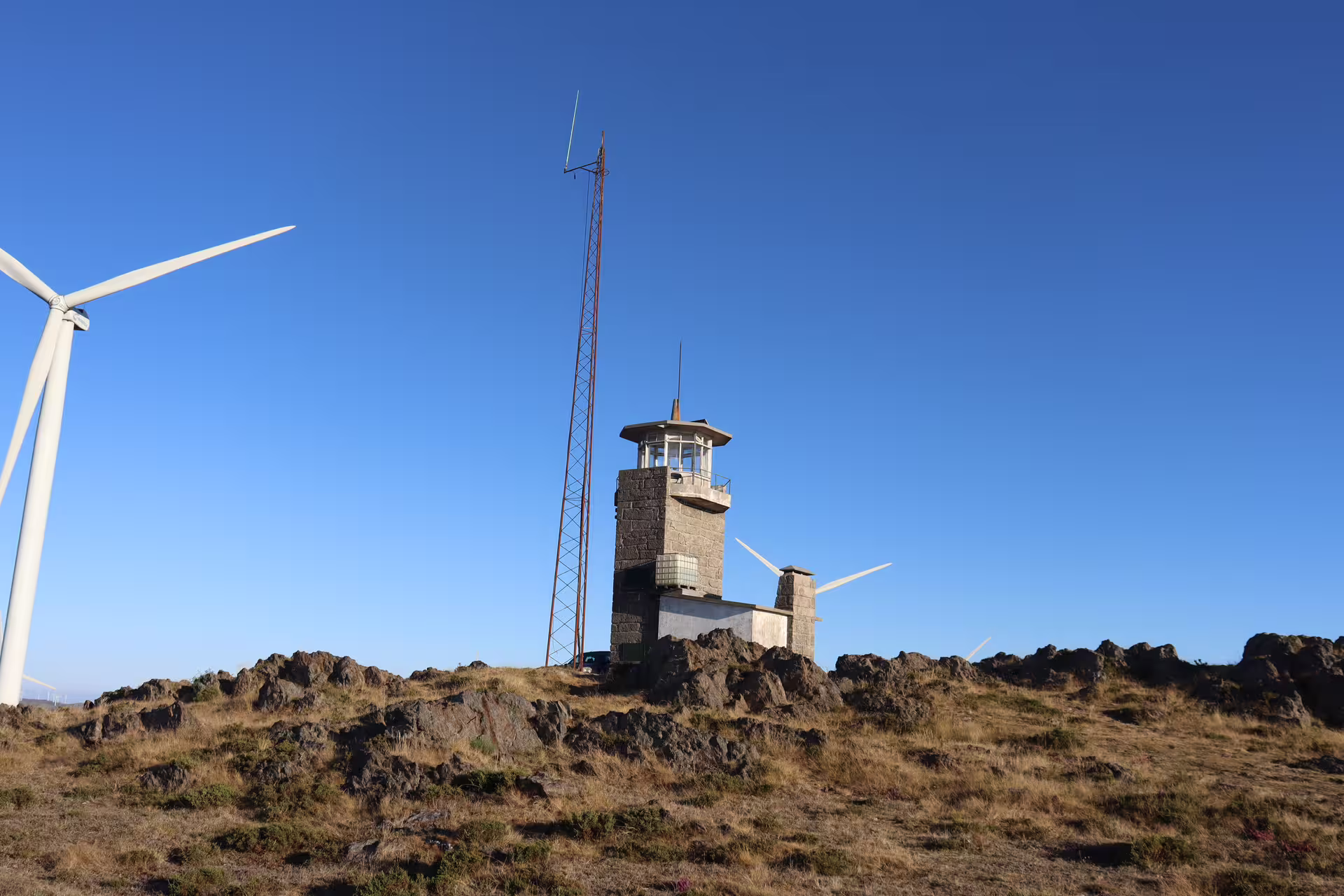 Scenic view of a stone tower and wind turbines under a clear blue sky, highlighting the Arouca 516 Bridge and Paiva Walkways tour.