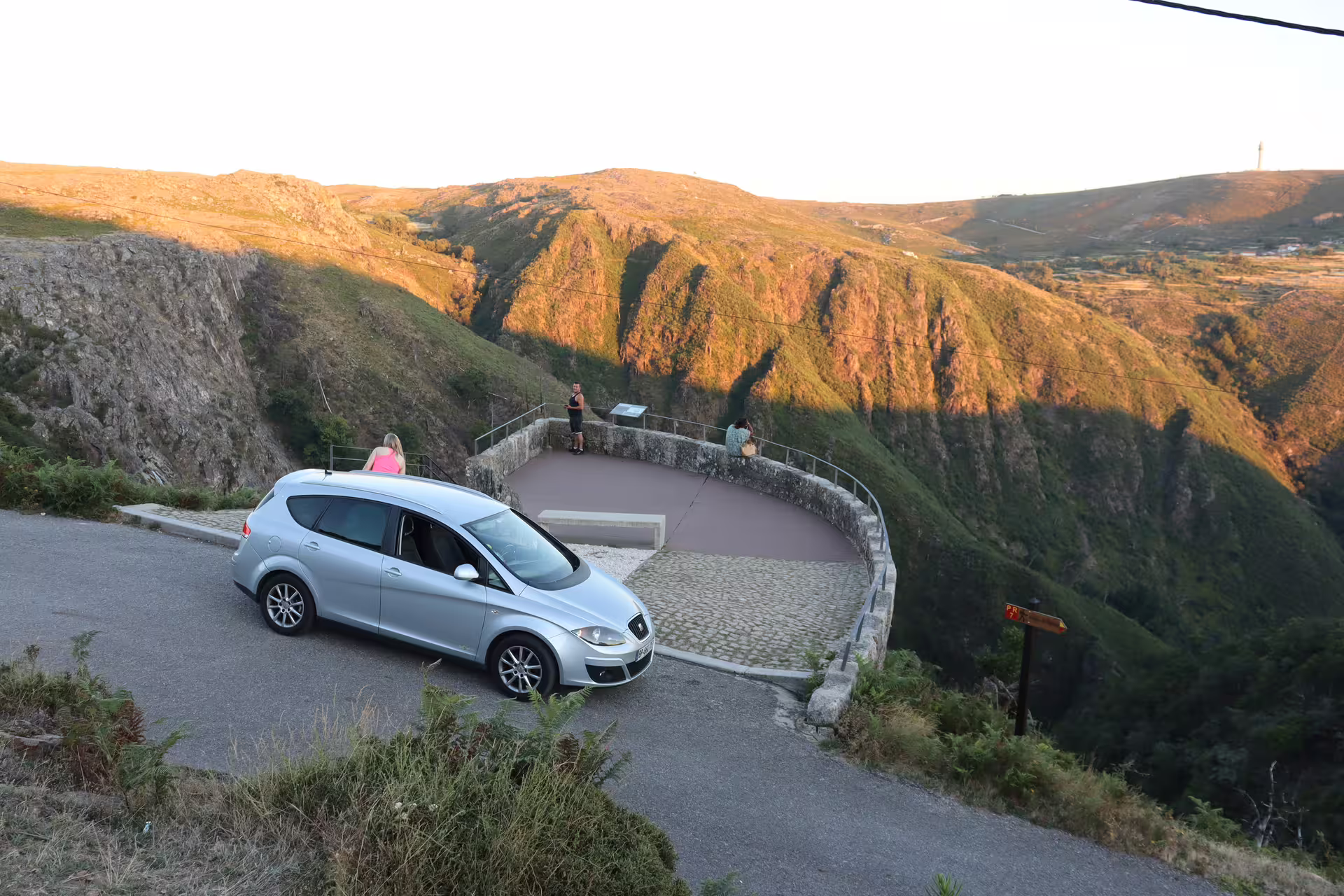 Scenic viewpoint overlooking lush valleys near Arouca 516 Bridge and Paiva Walkways, featuring a parked car and sunset hues.