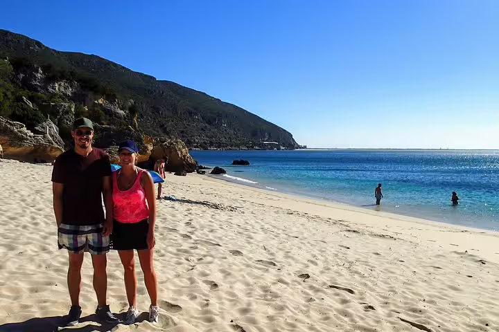 Couple enjoying a sunny day on Arrábida's pristine beach, perfect for snorkeling and savoring local wines amidst stunning coastal views.