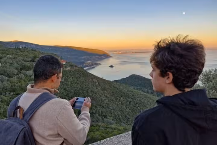 Two tourists enjoying a sunset view over Arrábida's scenic landscape on a private wine tour from Lisbon.