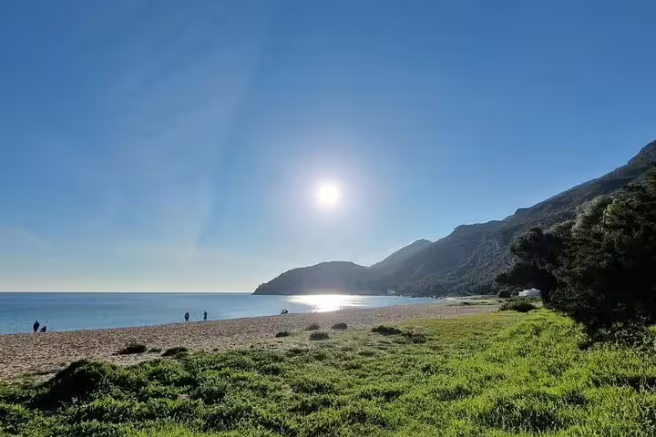 Scenic Arrábida beach with lush greenery and sunlit hills, perfect for a relaxing day trip with wine tasting and nature exploration.