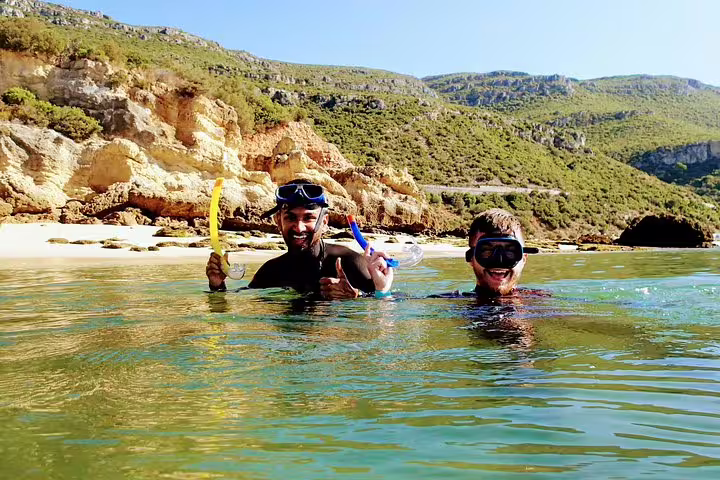 Two snorkelers enjoying clear waters and scenic cliffs during an Arrábida snorkeling adventure with transfer from Lisbon.