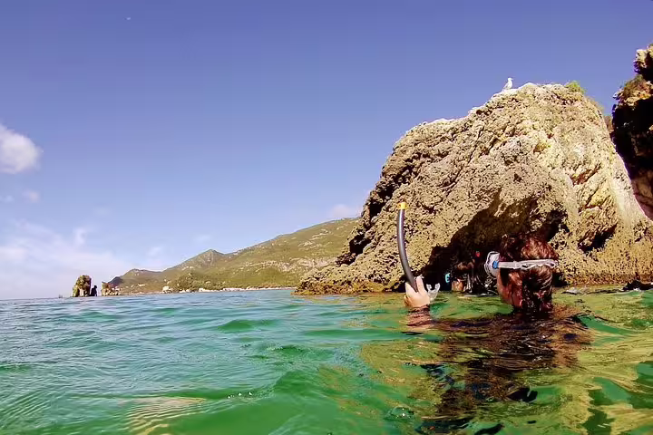Snorkeler explores vibrant waters near rocky formations in Arrábida, showcasing a scenic adventure with Lisbon transfers.