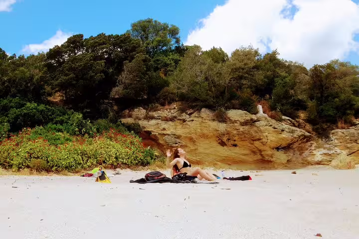 A woman relaxes on a sandy beach in Arrábida, surrounded by lush cliffs, ready for a snorkeling adventure from Lisbon.