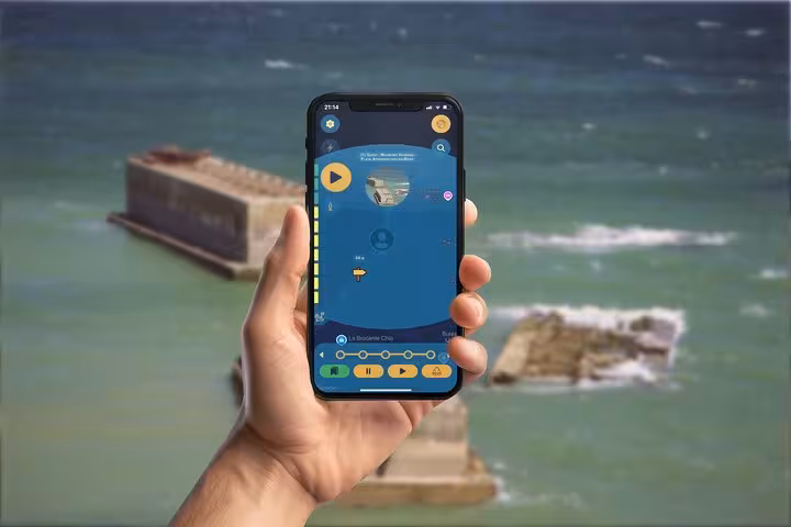 Hand holding smartphone with D-Day tour mobile game app, Arromanches beach ruins in background