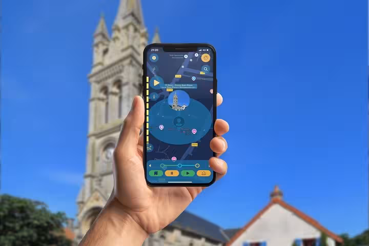 Hand holding smartphone with D-Day tour mobile game app in front of Arromanches church tower