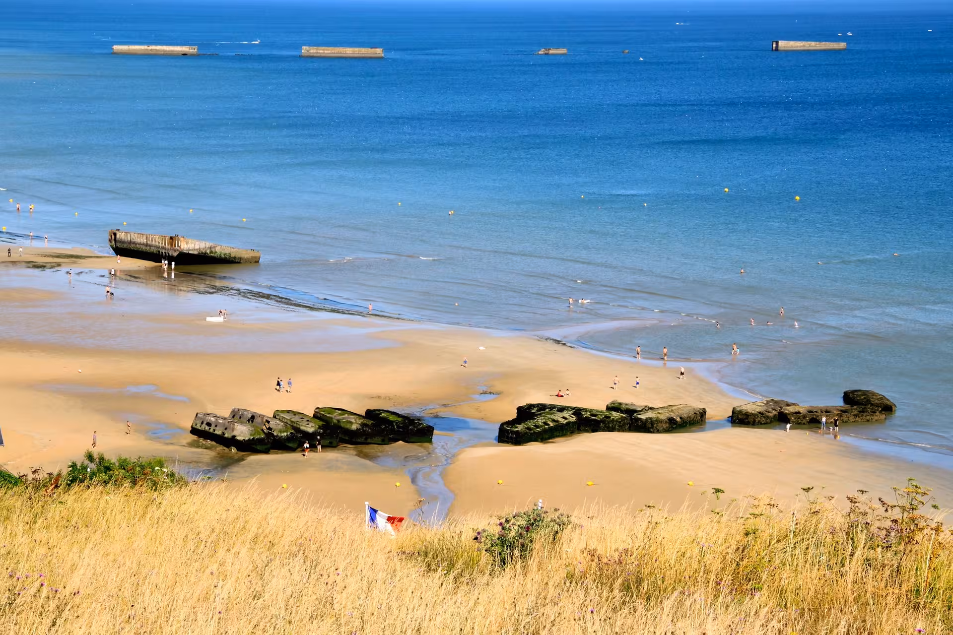 Aerial view of Arromanches Gold Beach with WWII Mulberry harbour remains and tourists on Normandy shore