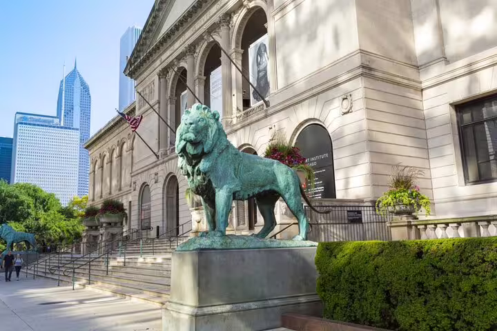 Bronze lion statue at the Art Institute of Chicago entrance with city skyline in background