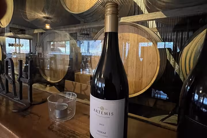 Bottle of Artemis Shiraz 2023 displayed in a Southern Highlands winery with wooden barrels in the background.