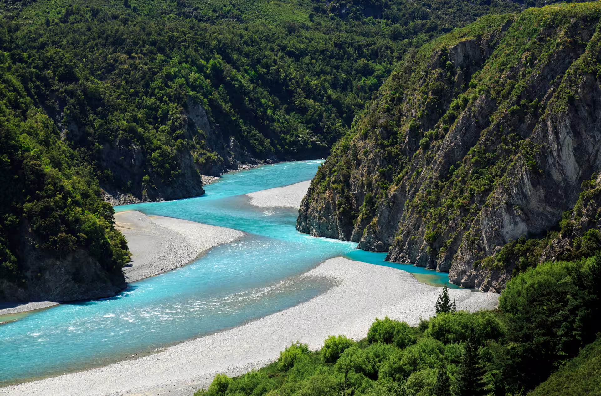 Vibrant turquoise river winding through lush green cliffs in Arthur's Pass, showcasing stunning alpine vistas.