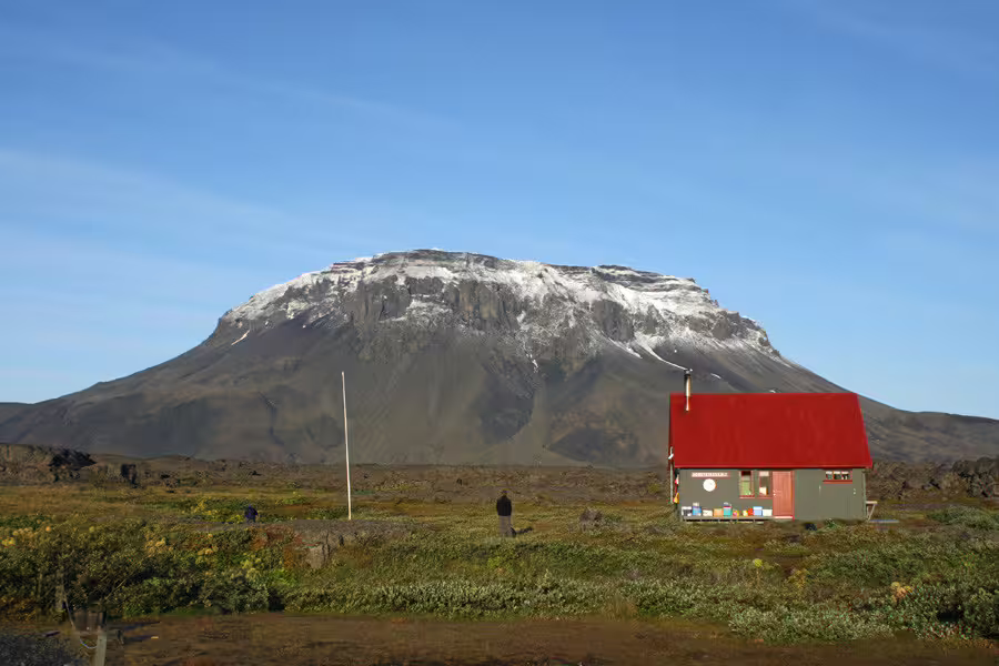 Red-roofed highland hut with flat-topped snow-dusted Herðubreið volcano in Askja Iceland highlands