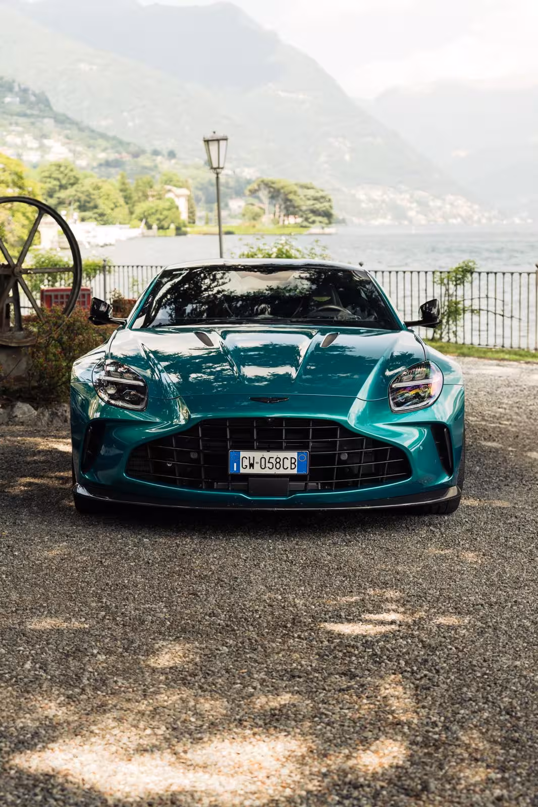 Emerald green Aston Martin supercar parked by Lake Como with mountain backdrop, Italian license plate