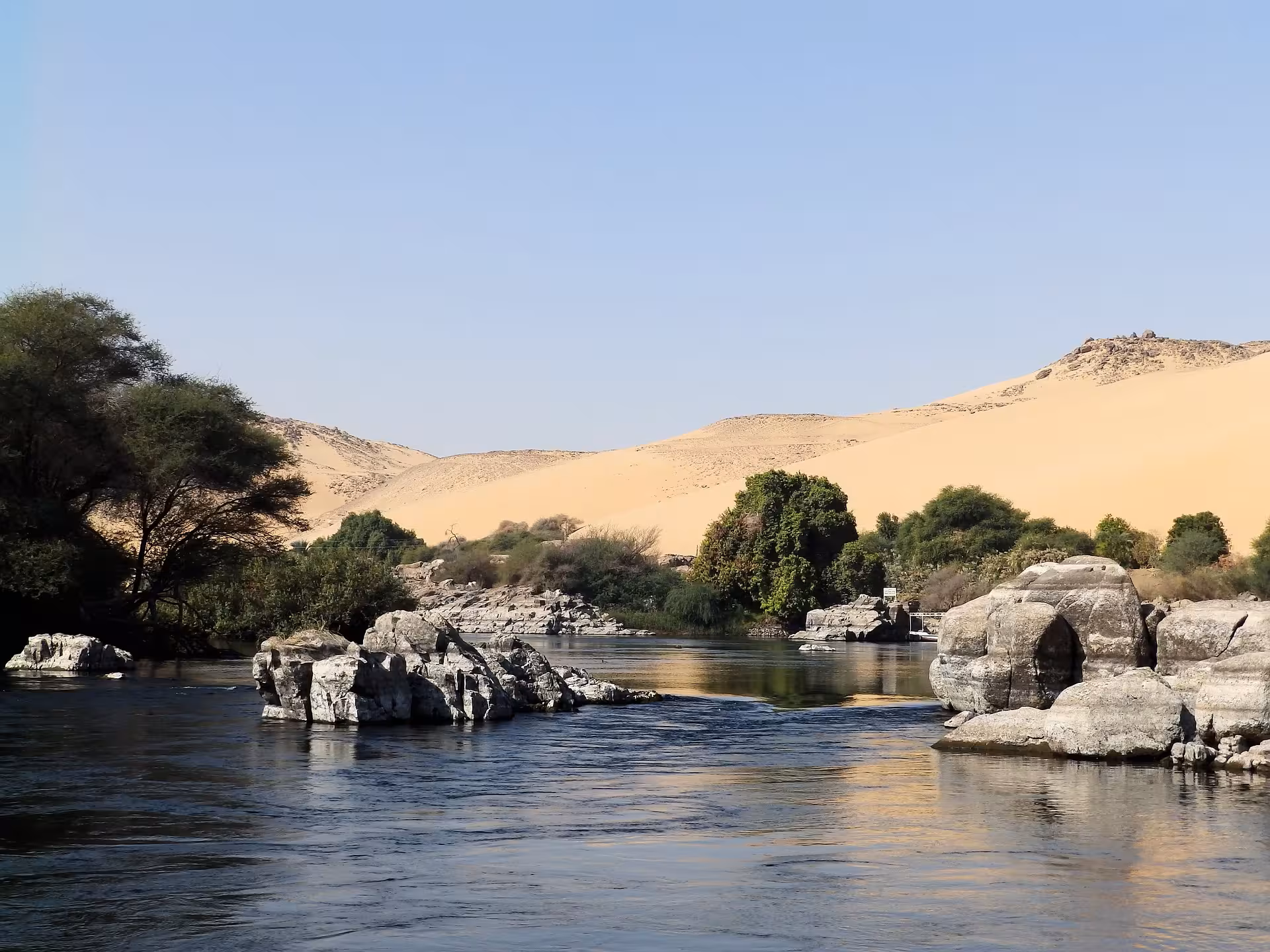 Rocky Nile River with lush greenery and golden sand dunes near Aswan, Egypt
