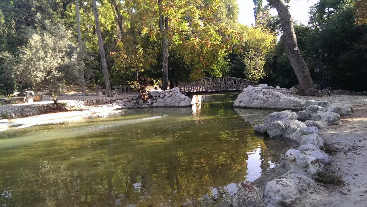Shaded park pond with wooden footbridge in Athens, a relaxing stop on Acropolis and Plaka walking tour