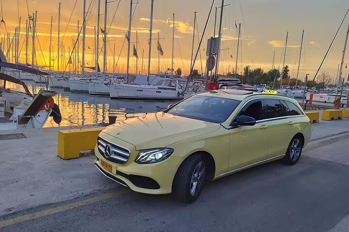 Luxury private transfer car for Athens Airport to city center parked by marina at sunset, premium chauffeur service