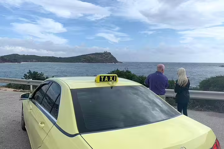 Couple enjoys scenic view of Cape Sounion's coastline from a taxi stop on a full or half-day trip from Athens.