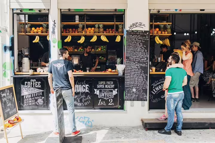 Athens small-group food tour stop at a fresh juice bar with fruit display and locals ordering drinks